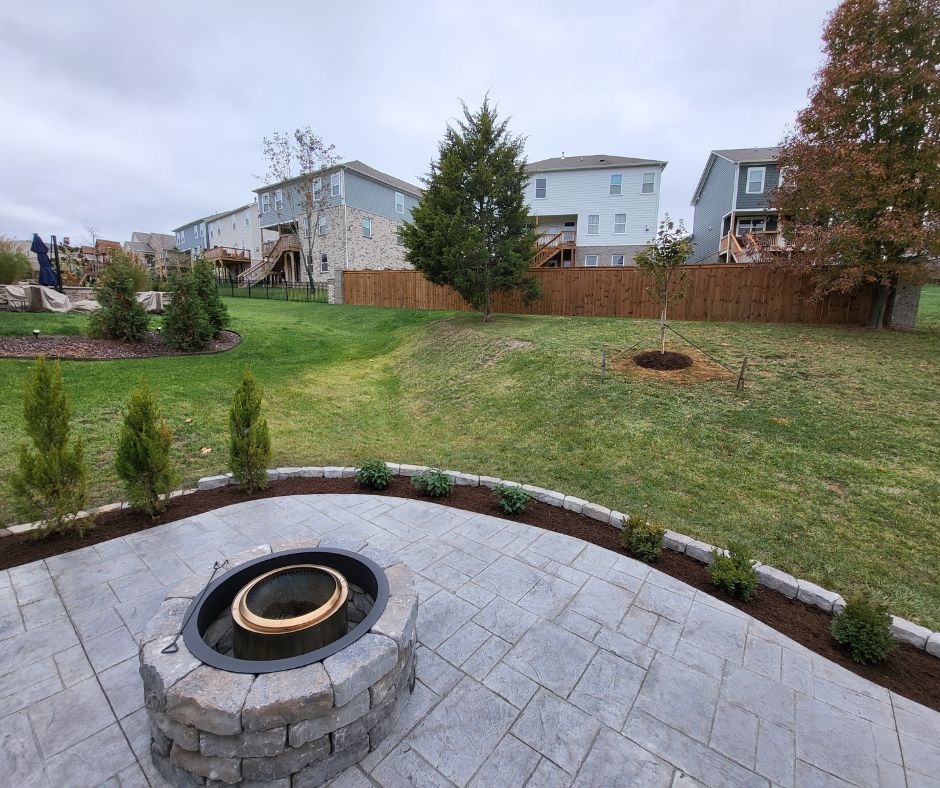 A beautifully landscaped backyard featuring patio pavers, a fire pit, newly planted trees, and a well-maintained lawn. Located in Spring Hill, TN
