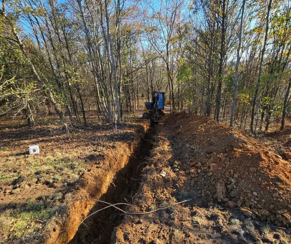 A shallow ditch being dug for electrical wiring installation in a lawn by Cutting Edge team members.